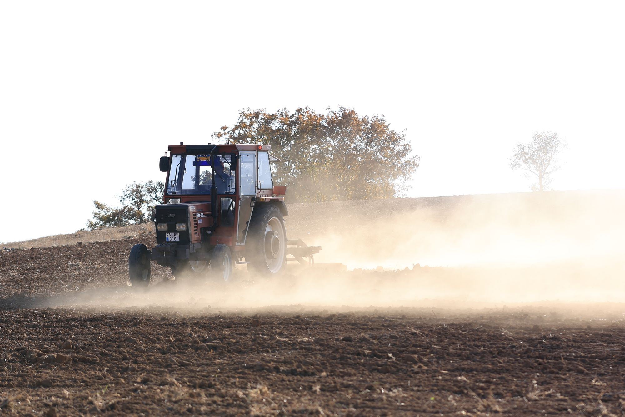 A red tractor working a dusty field ahead of planting